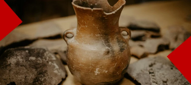 Vase en poterie ancienne et fragments de silex exposés sur une table au Jardin archéologique