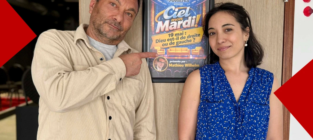 Photo de Bruno Romier et d'une femme posant à côté d'une affiche pour le talk-show "Ciel, mon mardi !" à la Comédie d'Amiens. L'affiche annonce un débat le 19 mai avec la thématique "Dieu est-il de droite ou de gauche ?" présenté par Mathieu Wilheim. Bruno Romier pointe du doigt l'affiche.