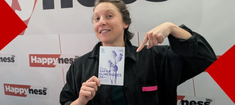 Une femme souriante dans les studios d'Happyness Radio présente et pointe du doigt le programme du festival « Safra Numériques », qui se déroule du 24 au 28 mars. Elle porte une chemise noire et se tient devant un mur habillé du logo de la radio Happyness. L'image est encadrée par des éléments graphiques rouges en diagonale dans les coins.