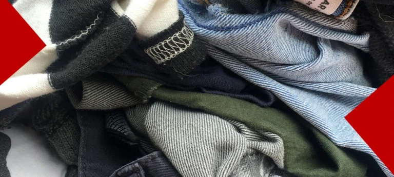 Un gros plan sur un tas de vêtements de seconde main entassés, illustrant l'upcycling et la circularité textile. On y distingue des jeans en denim bleu clair et foncé, des tricots rayés noirs et blancs, et des textiles verts et gris. Deux triangles rouges décorent les angles supérieurs et inférieurs.