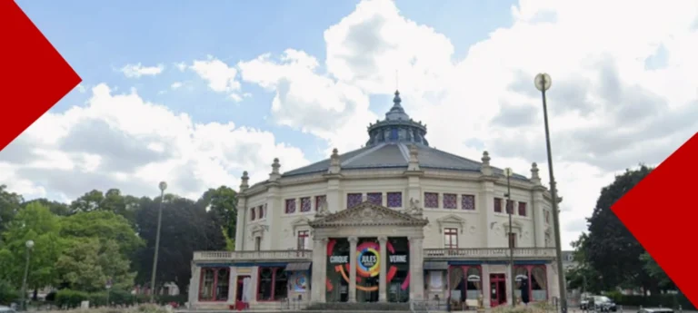 Vue extérieure du Cirque Jules Verne à Amiens sous un ciel nuageux, montrant son architecture circulaire en pierre et son entrée monumentale avec l'affiche du Pôle National Cirque.