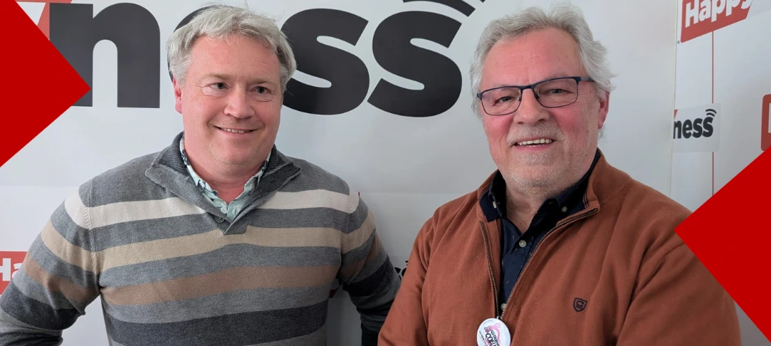Deux hommes souriants posent côte à côte devant un mur blanc arborant le logo « Happyness ». L'homme à gauche porte un pull à rayures horizontales grises, beiges et bleues, tandis que l'homme à droite porte une veste boutonnée de couleur rouille et des lunettes. Des formes géométriques rouges encadrent les coins de l'image.