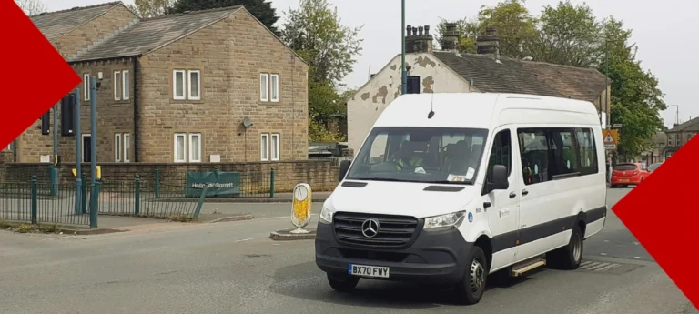 Une camionnette Mercedes-Benz blanche circulant dans une rue pavée d'une ville britannique. En arrière-plan, on aperçoit des maisons traditionnelles en pierre et un panneau publicitaire « Holland & Barrett ». L'image est encadrée par deux formes géométriques rouges dans les coins opposés.