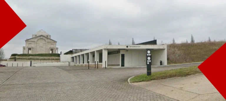 Vue du centre d'information moderne de l'Australian National Memorial en béton blanc situé au pied d'un imposant en pierre claire, sous un ciel couvert.