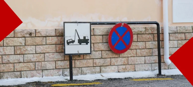 : Une vue horizontale montre deux panneaux de signalisation fixés sur une barre métallique noire devant un mur en briques beiges. À gauche, un panneau carré blanc affiche le pictogramme noir d'une dépanneuse remorquant une voiture. À droite, un panneau circulaire bleu bordé de rouge est barré d'une croix rouge, indiquant une interdiction de stationner et de s'arrêter. Le sol présente des traces de neige et un marquage jaune au sol. Deux larges formes géométriques rouges encadrent les coins supérieurs gauche et inférieurs droit de l'image.