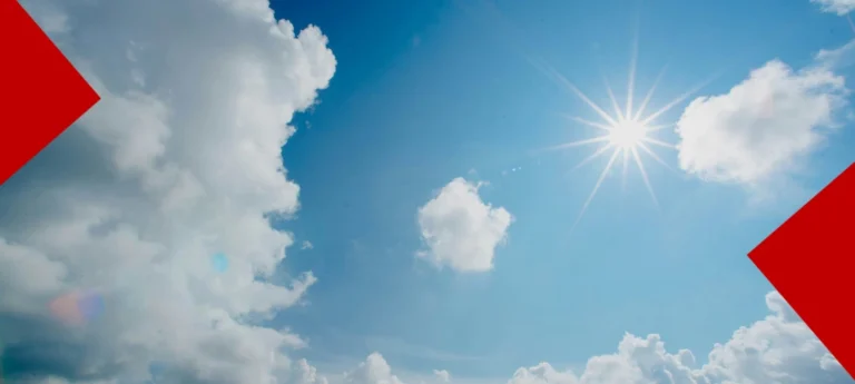 Un ciel bleu parsemé de nuages blancs avec un soleil éclatant au centre. Deux formes géométriques rouges (chevrons) encadrent les coins supérieurs gauche et inférieurs droit de l'image.