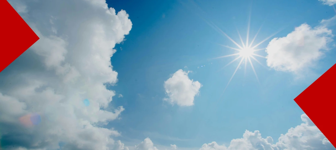 Un ciel bleu parsemé de nuages blancs avec un soleil éclatant au centre. Deux formes géométriques rouges (chevrons) encadrent les coins supérieurs gauche et inférieurs droit de l'image.
