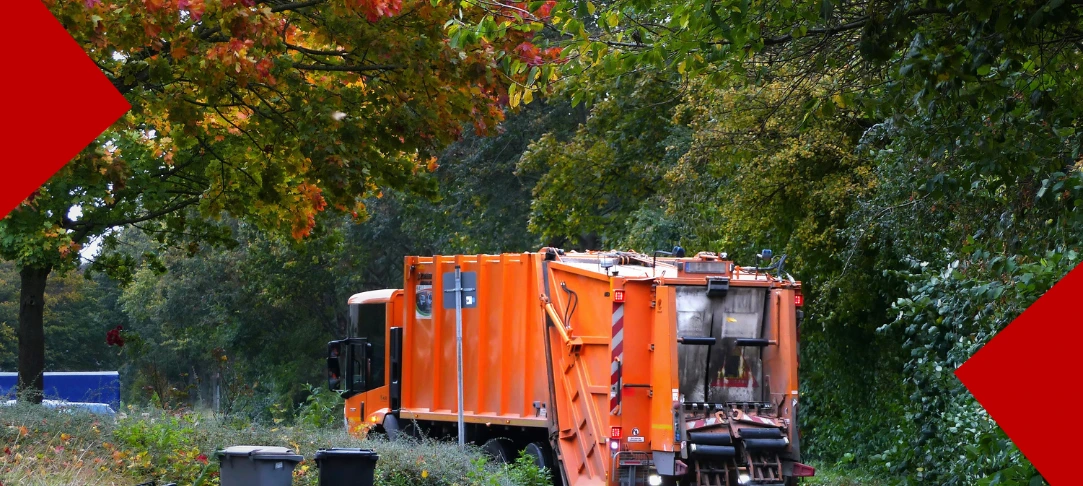 Arrière d'un camion poubelle orange de tri sélectif en cours de collecte, garé sur le bord d'une route arborée avec un arbre aux feuilles d'automne et une poubelle à l'arrière-plan. Deux éléments graphiques rouges sont présents dans les coins supérieurs et inférieurs.