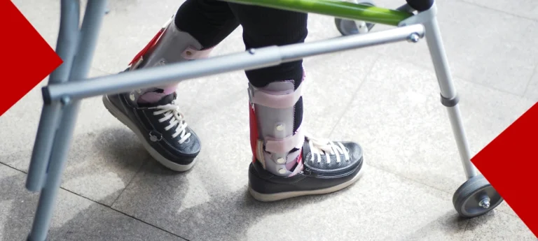 Vue en gros plan des jambes d'un enfant utilisant un déambulateur médicalisé. L'enfant porte des baskets noires montantes adaptées par-dessus des orthèses de marche (attelles pédiatriques) de couleur grise et rose. Le cadre du déambulateur est gris avec une barre supérieure verte. Des formes géométriques rouges encadrent les coins de l'image.