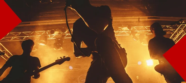 Silhouette d'un chanteur de métal sur scène micro à la main, entouré d'un guitariste et d'un bassiste, dans une ambiance de concert énergique avec un éclairage orange chaud et de la fumée de scène.