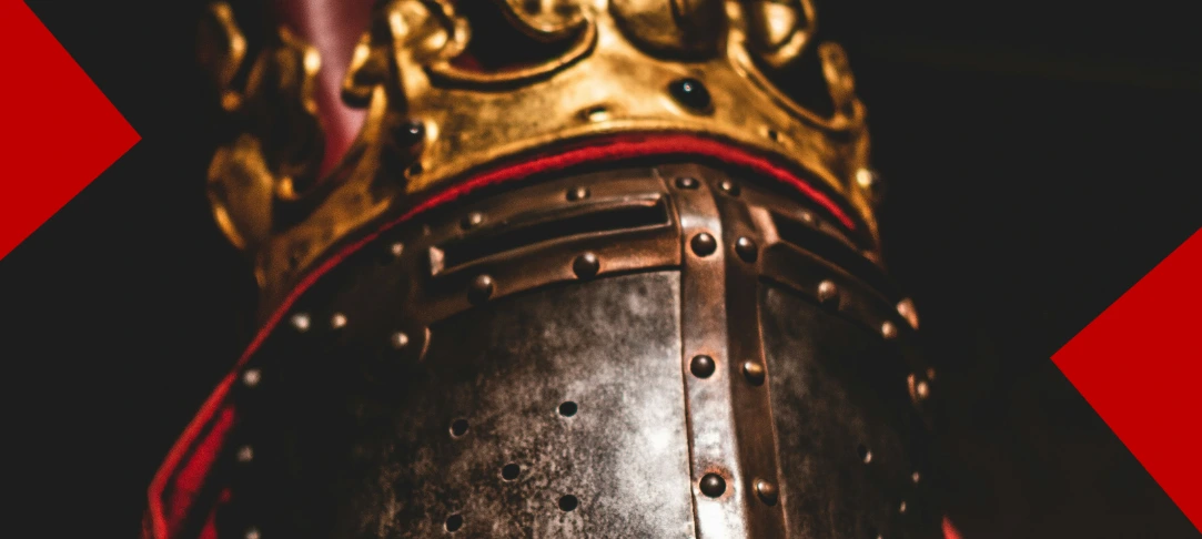 Gros plan sur un heaume de chevalier en métal martelé, surmonté d'une couronne dorée ornée de pierres sombres. L'image est encadrée par deux formes géométriques rouges sur un fond noir.