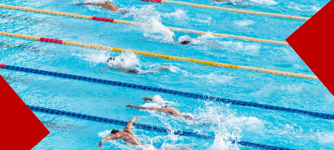 Une vue aérienne de nageurs en pleine compétition dans une piscine olympique. Les athlètes tracent leur chemin dans des couloirs séparés par des lignes de flotteurs jaunes et bleus, créant des éclaboussures d'eau blanche et vive. Deux larges formes géométriques rouges encadrent les coins inférieurs gauches et supérieurs droits de l'image.